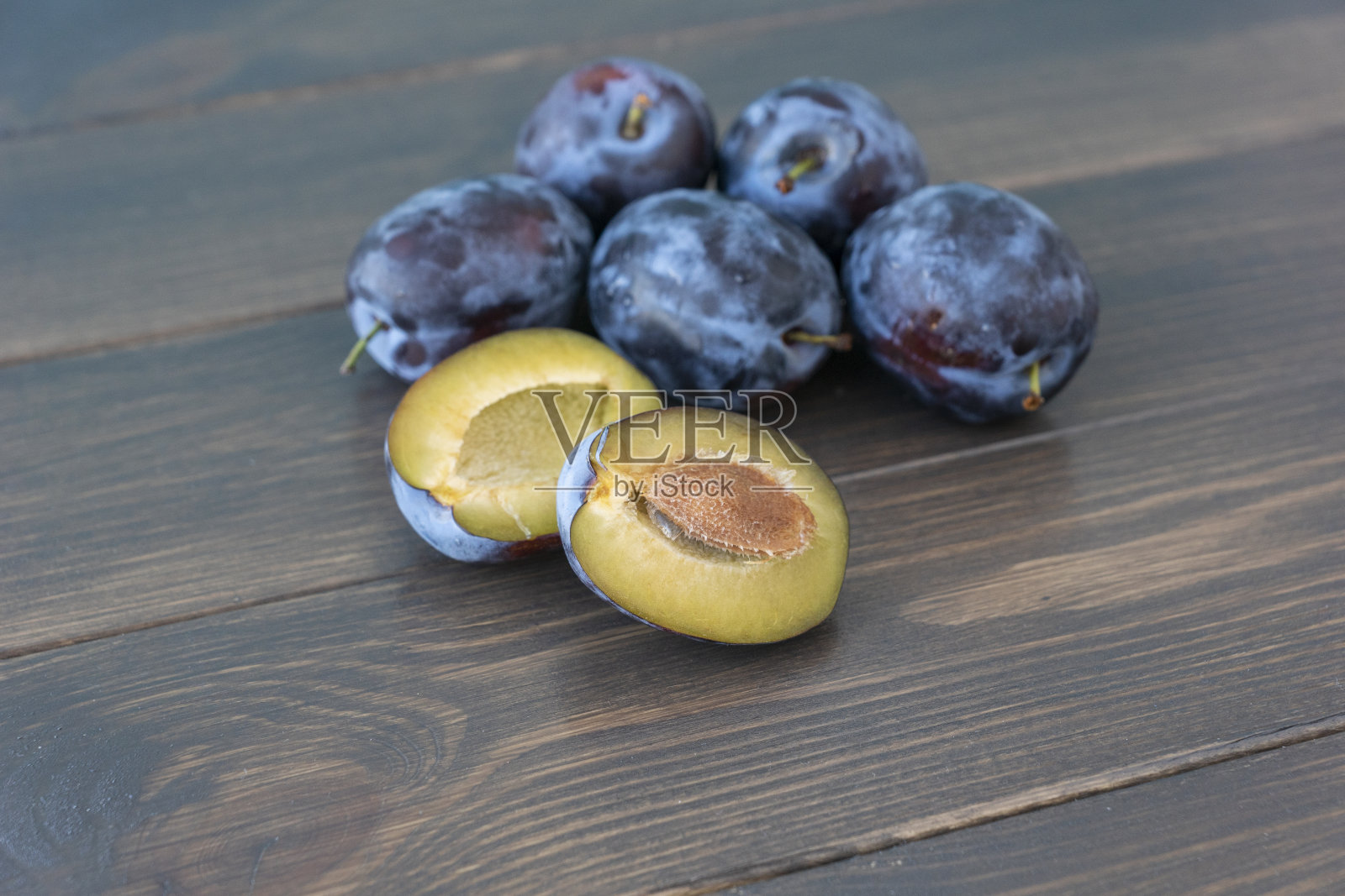 几个成熟的李子躺在深色的木头背景上的特写图像,一个李子被切成两半。照片摄影图片