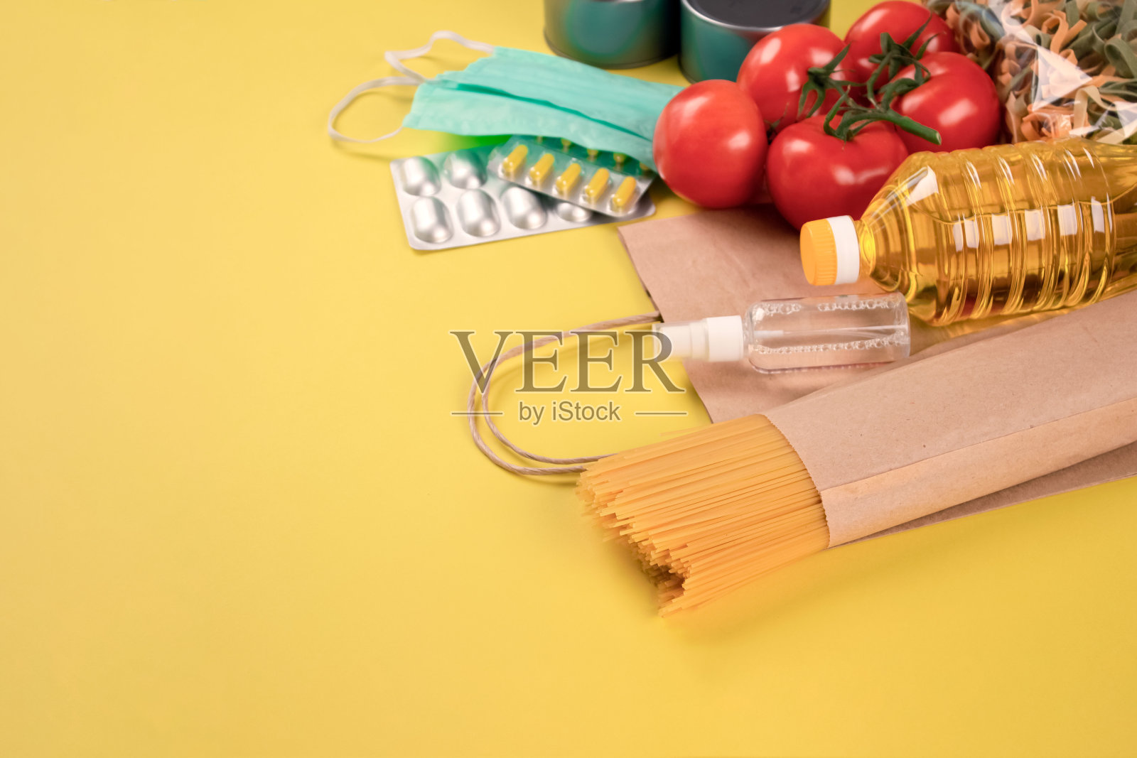 捐赠的食品和药物,黄色背景的纸袋与copyspace -意大利面,新鲜蔬菜,油,口罩,药片和消毒喷雾。捐赠或送餐理念照片摄影图片