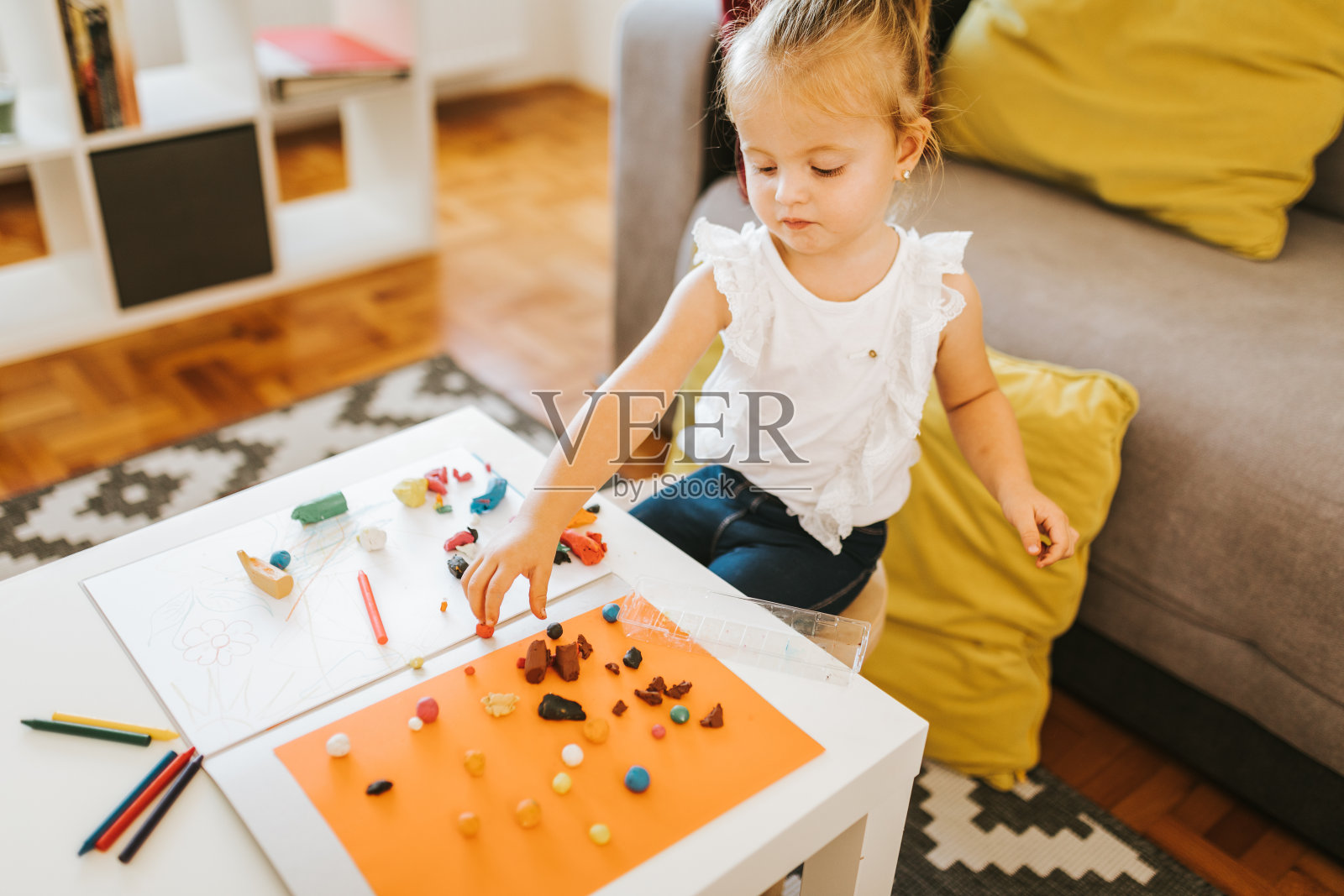 快乐的小女孩坐在家里玩橡皮泥。照片摄影图片