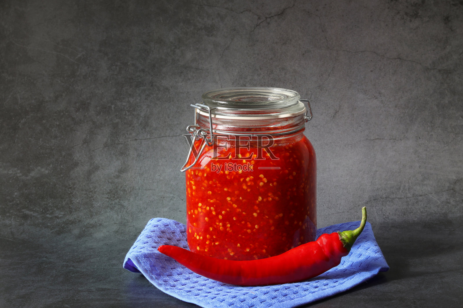 磨碎的红辣椒和番茄在一个玻璃罐在黑暗的背景。一种在家里用胡椒和番茄做成的辣味调料。家乡菜。照片摄影图片