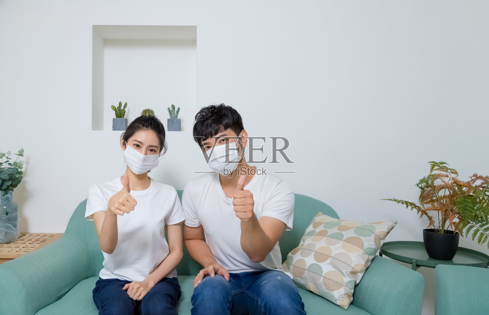 亚洲夫妇戴着防护口罩,在家里竖起大拇指。照片摄影图片
