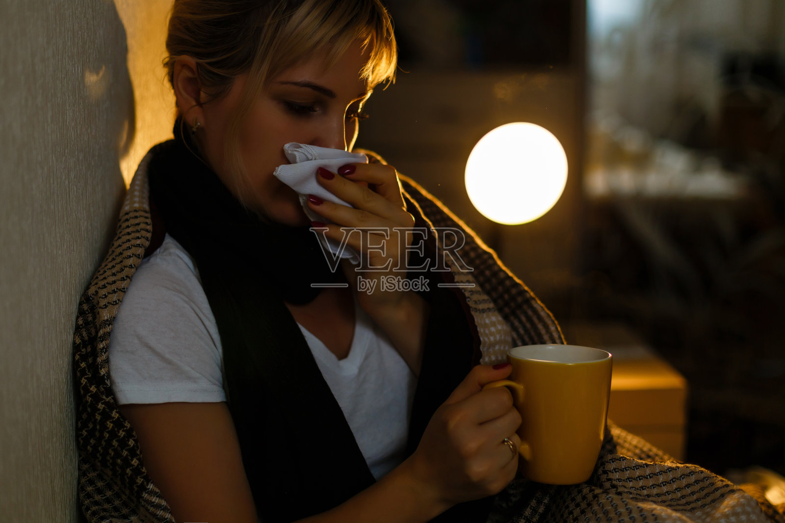 生病的女人,给你一杯茶。年轻沮丧的生病妇女在针织围巾拿着一杯茶躺在床上的特写图像。感觉不好。照片摄影图片