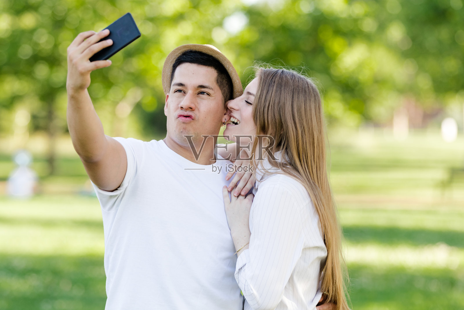 一对年轻情侣在公园里用手机自拍。拉丁男人和白人女人照片摄影图片