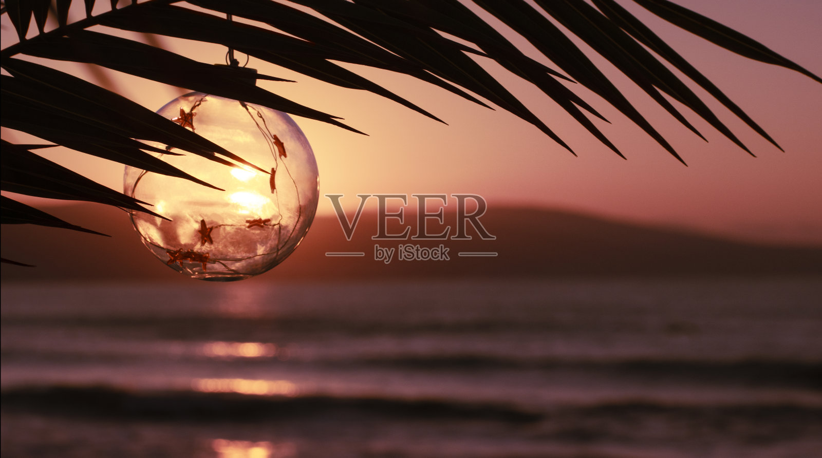 圣诞快乐,并附上新年贺卡。圣诞装饰玻璃球在日落的棕榈枝在海上。新年假期去温暖的国家旅游。横幅,复制空间照片摄影图片