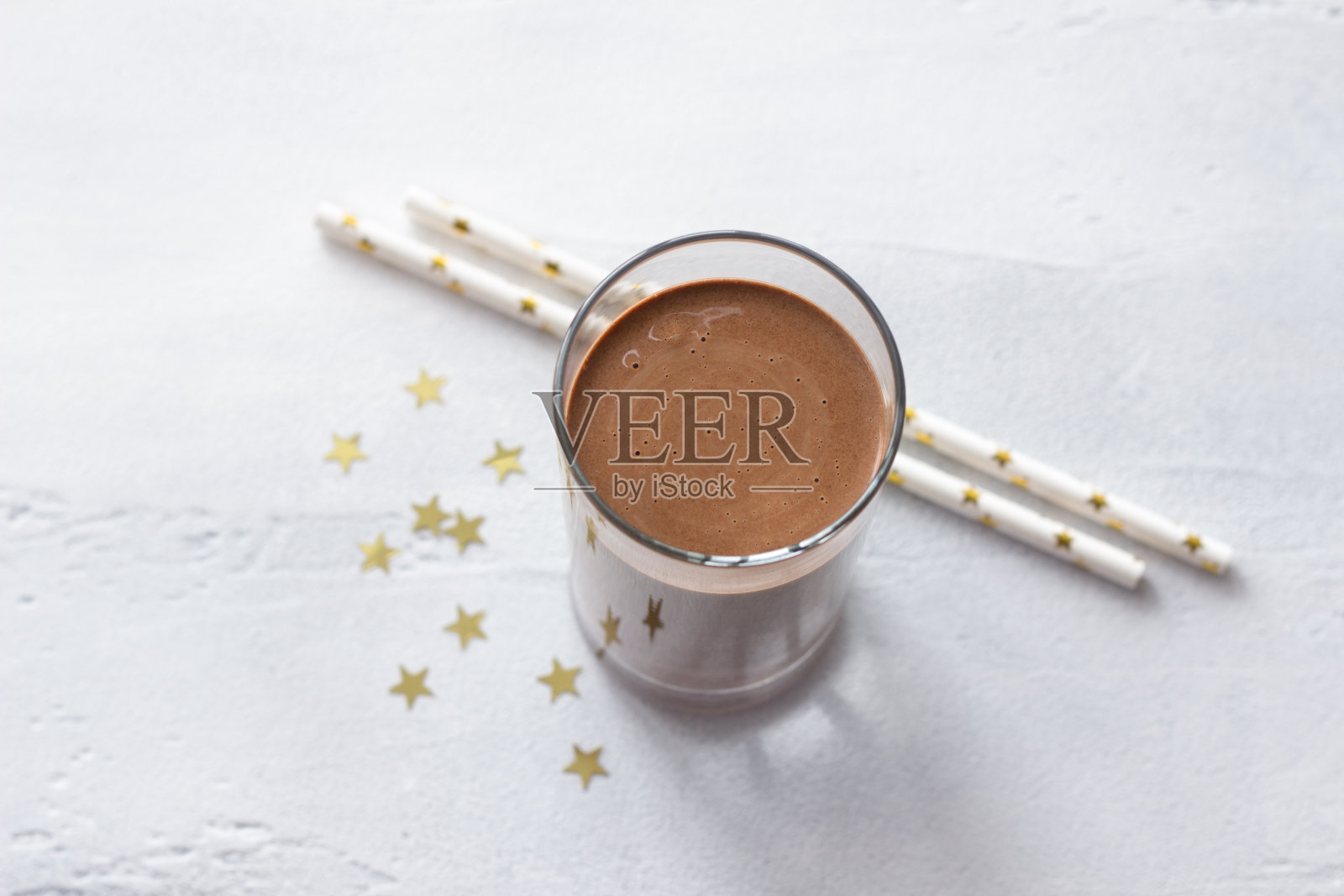 在浅灰色的背景上,点缀着节日装饰的巧克力椰奶、金色的五彩纸屑和派对喝吸管照片摄影图片