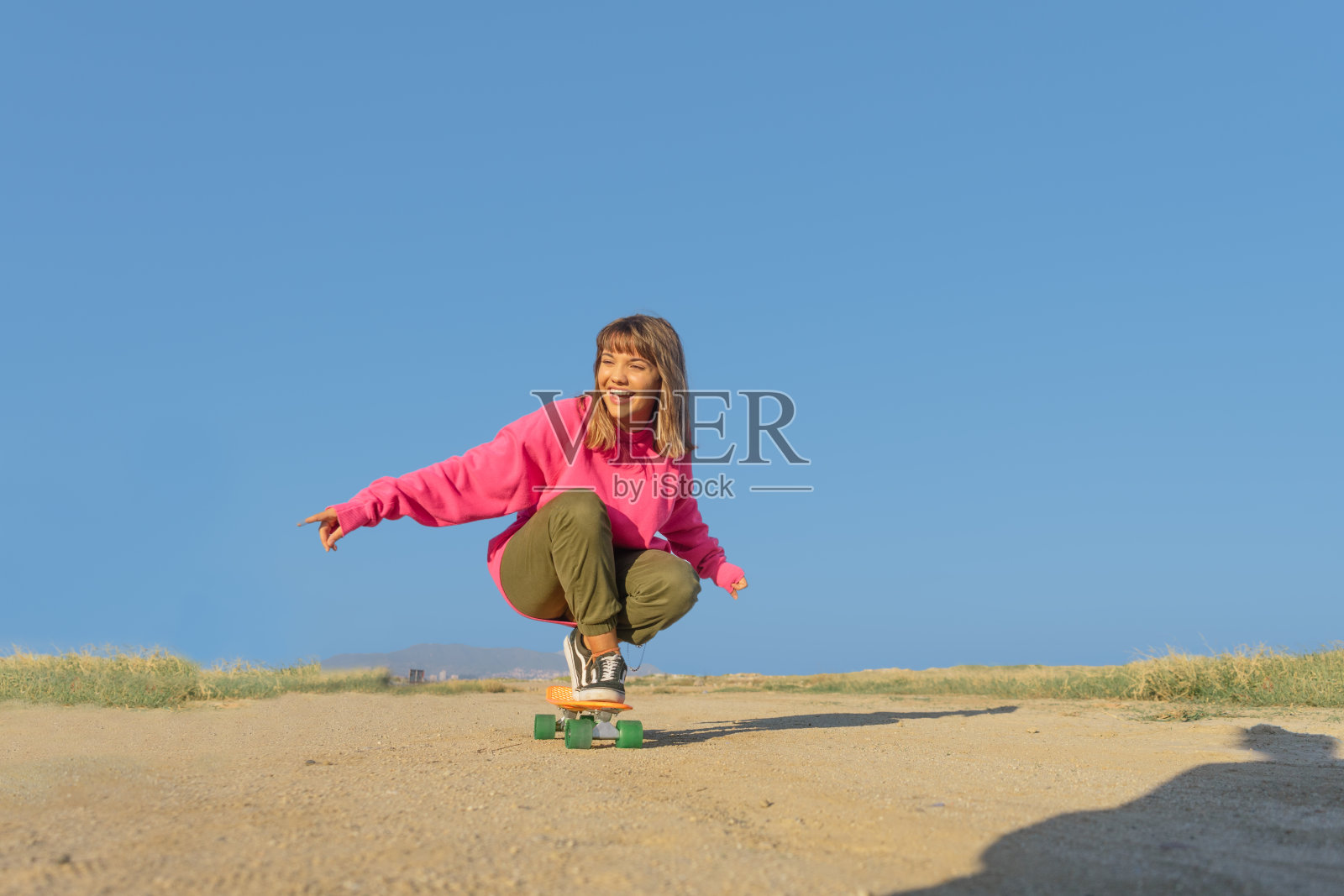 穿着粉色运动衫的年轻女子在人行道上玩滑板照片摄影图片