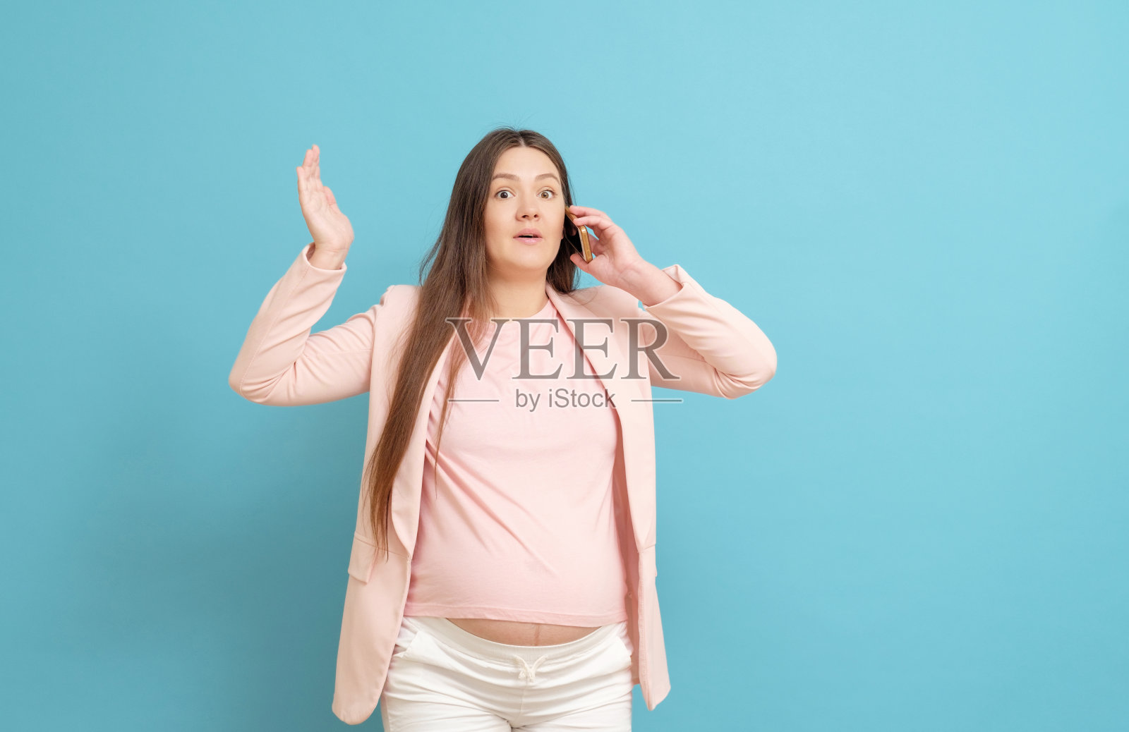 惊恐的年轻孕妇在蓝色背景下被手机呼叫,羊水排出,开始临产过程照片摄影图片