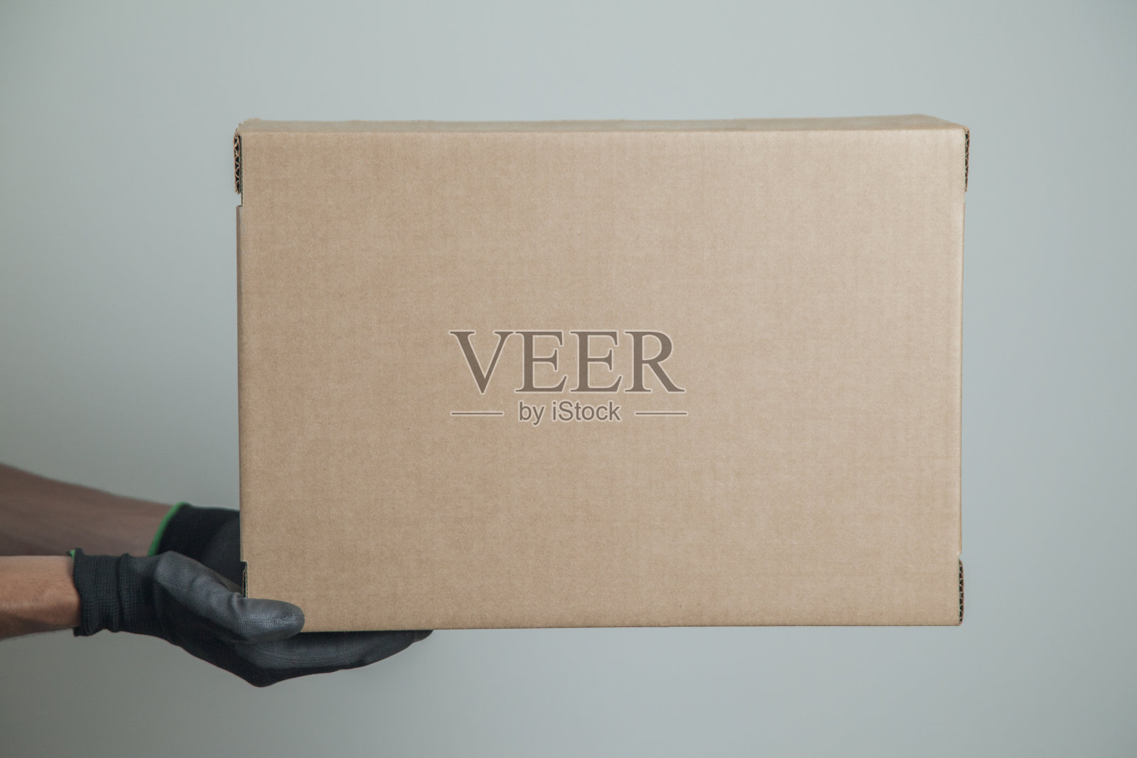 在灰色背景上,一个戴着黑色手套的男人拿着一个纸板箱运送产品照片摄影图片