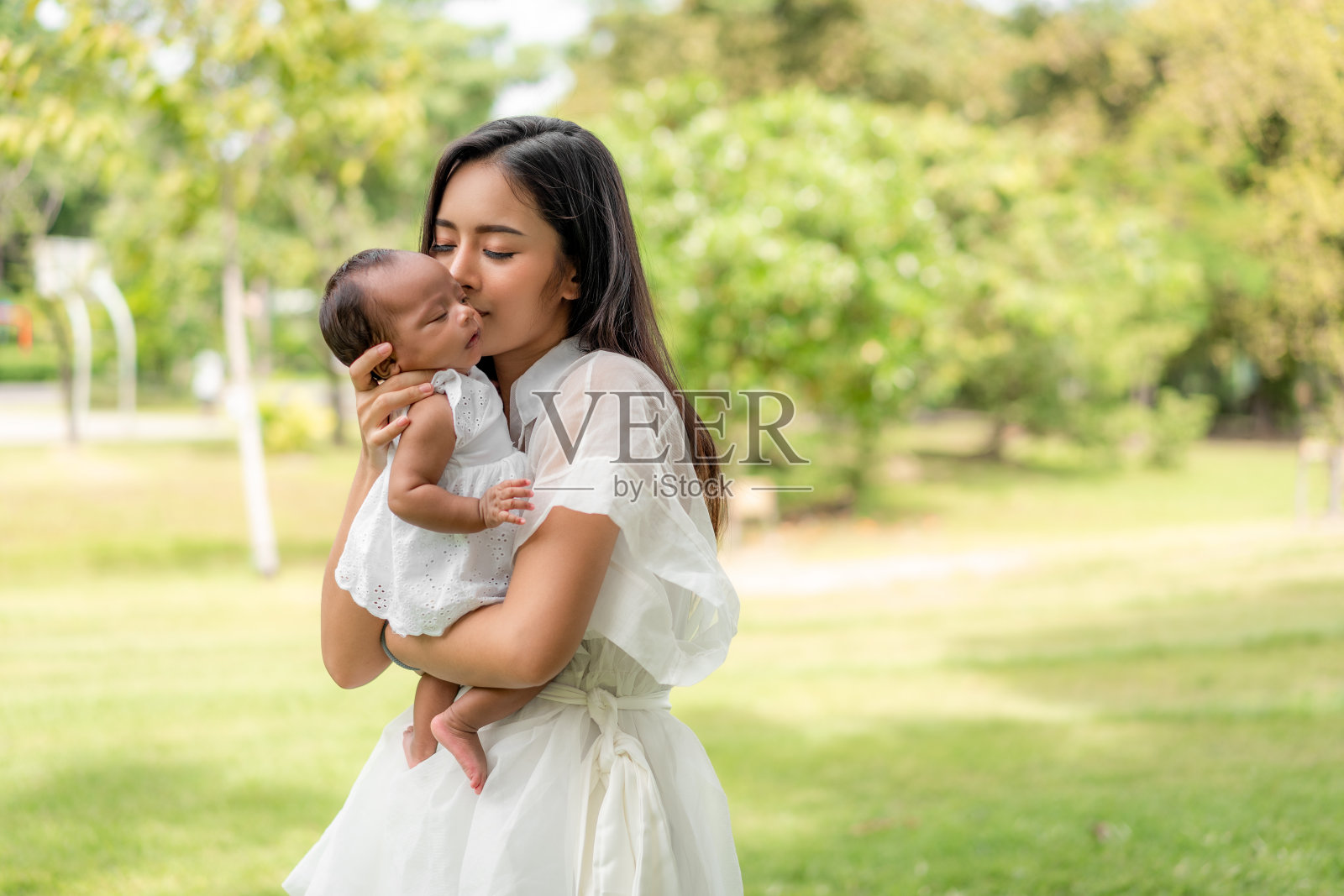 亚洲年轻美丽的母亲抱着她的新生儿正在睡觉,感觉与爱和轻轻触摸,然后坐在公园的绿色草地上照片摄影图片