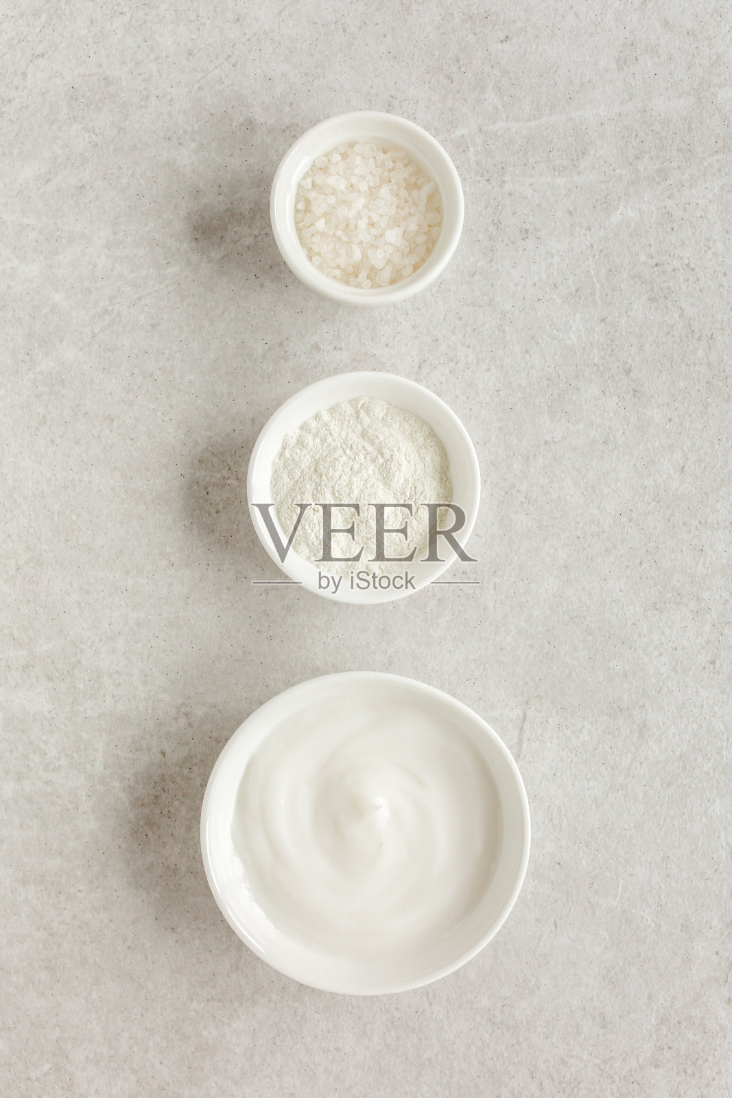 三种不同的天然水疗化妆品在一个碗:面霜,化妆粘土,海盐在灰色大理石的背景。护肤概念照片摄影图片