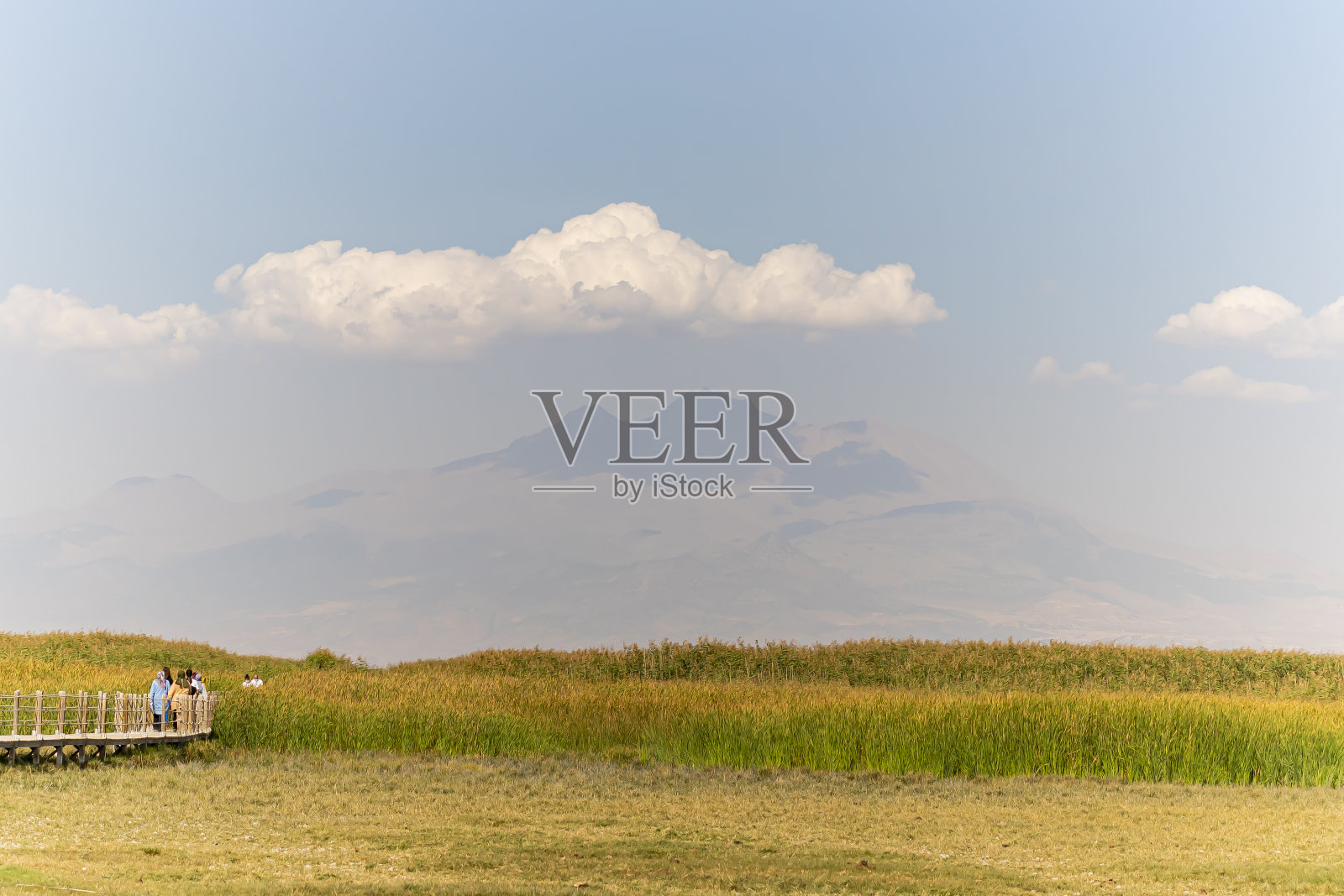 人们走在木桥上的芦苇和Erciyes山。照片摄影图片