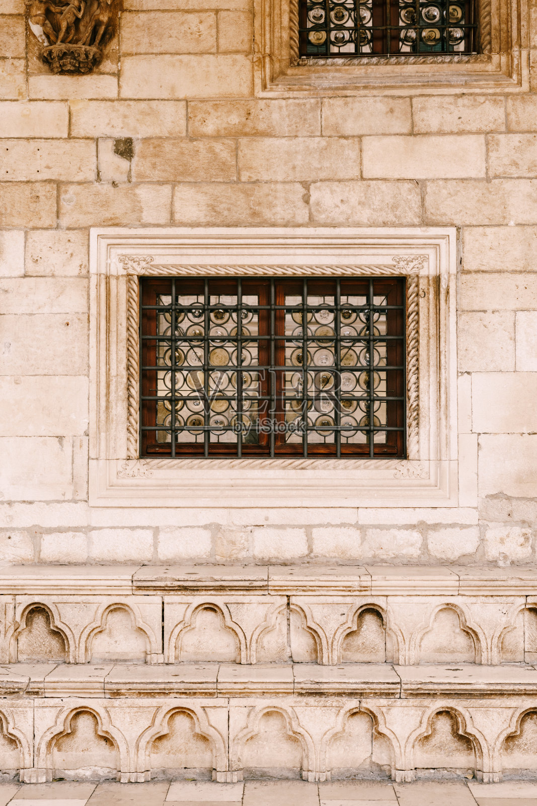 房子的石墙上有金属格子,后面是带有图案的彩色玻璃窗。照片摄影图片