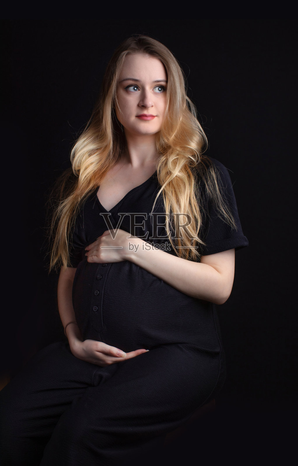 这是一幅以黑色为背景拍摄的快乐的、漂亮的年轻怀孕妈妈的漂亮画像。有足够的空间放白纸照片摄影图片