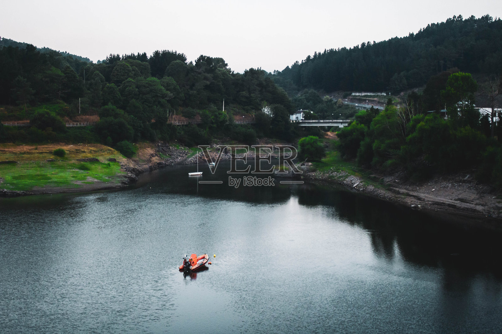 船在河中央,四周环绕着树木,映衬着多云的天空照片摄影图片