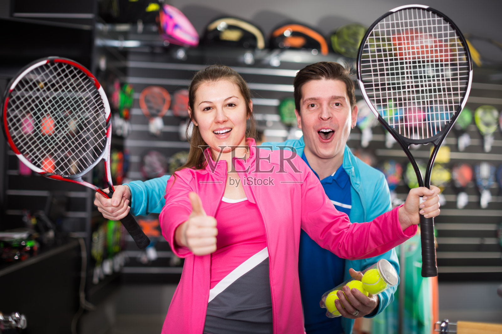 一对穿着运动服的年轻夫妇正在商店里展示新的火箭和网球照片摄影图片