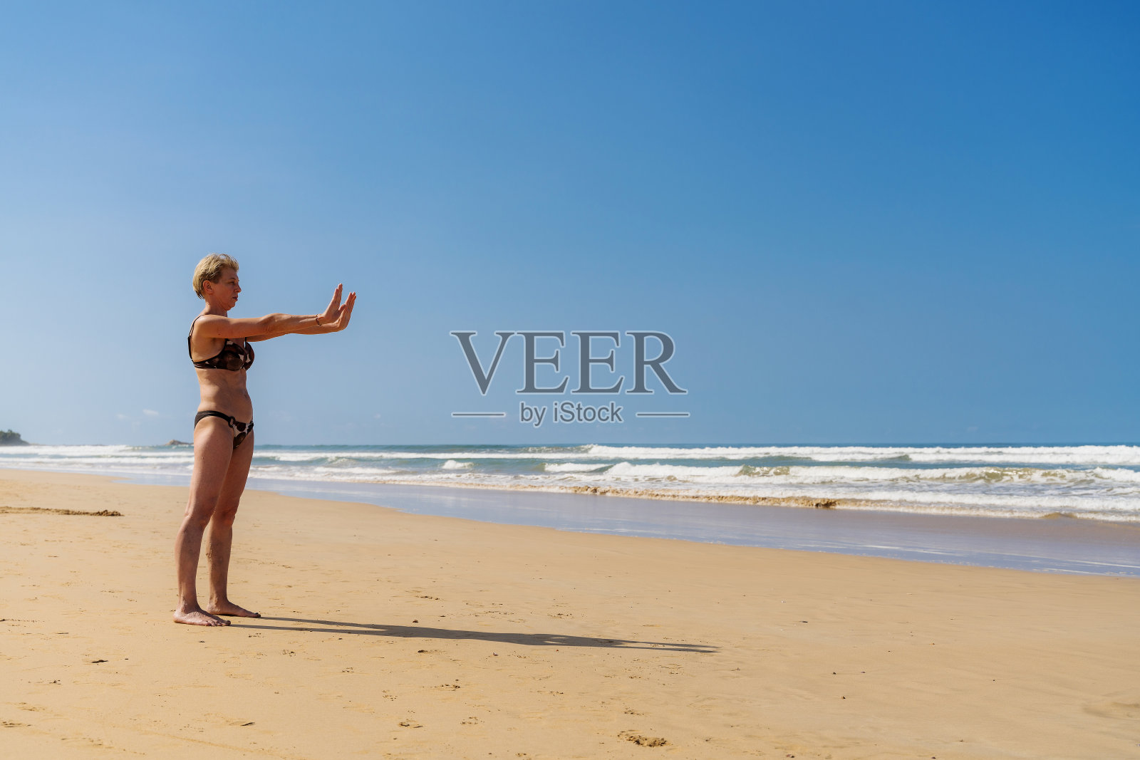 52岁的资深欧洲女性,独自旅行,在热带沙滩上做瑜伽健身练习。照片摄影图片