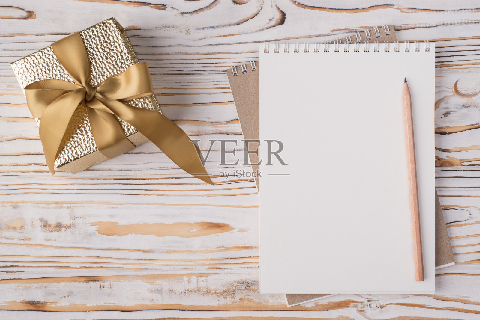 上面的俯视视图平放一张空白笔记本铅笔和金色礼物盒的照片孤立在与copyspace的浅色木制背景上照片摄影图片