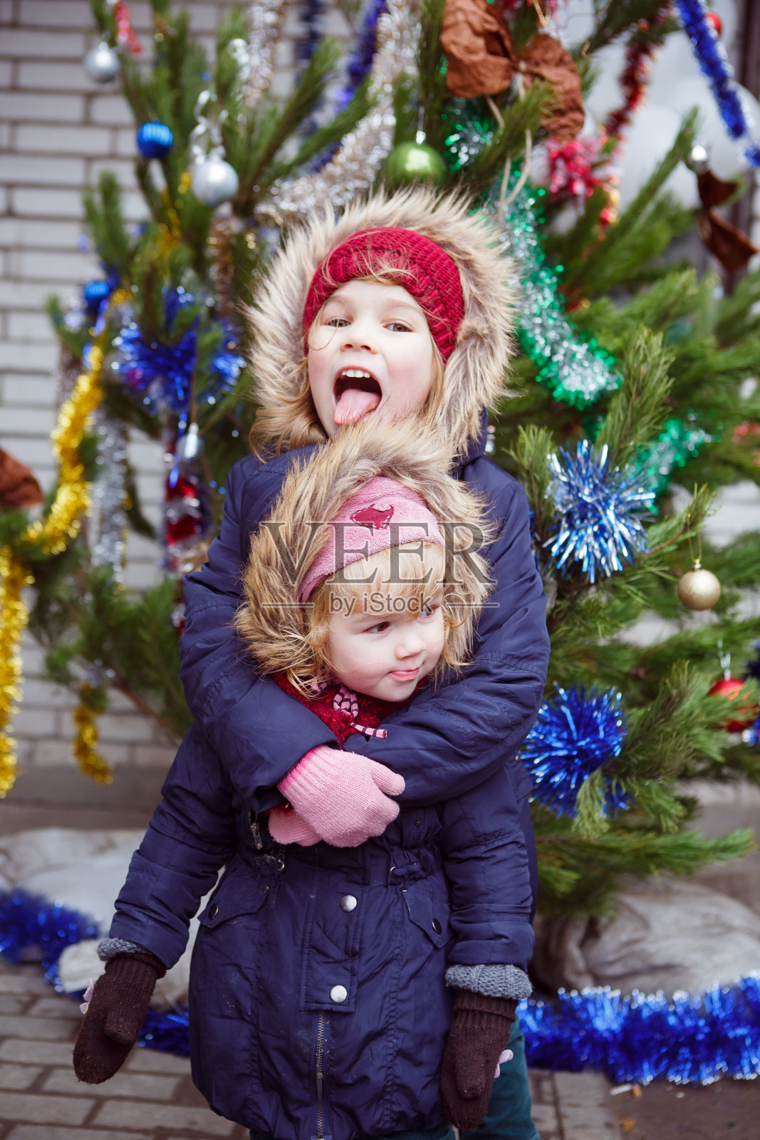 有趣的女孩站在圣诞树附近的街道上。照片摄影图片