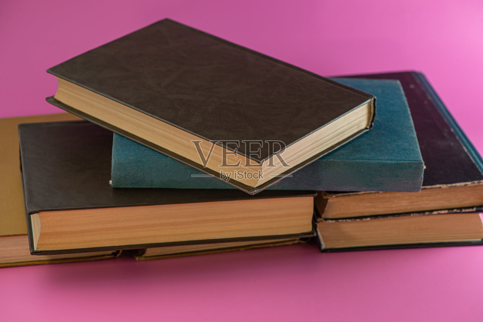 粉红色的背景上是一堆旧书。照片摄影图片