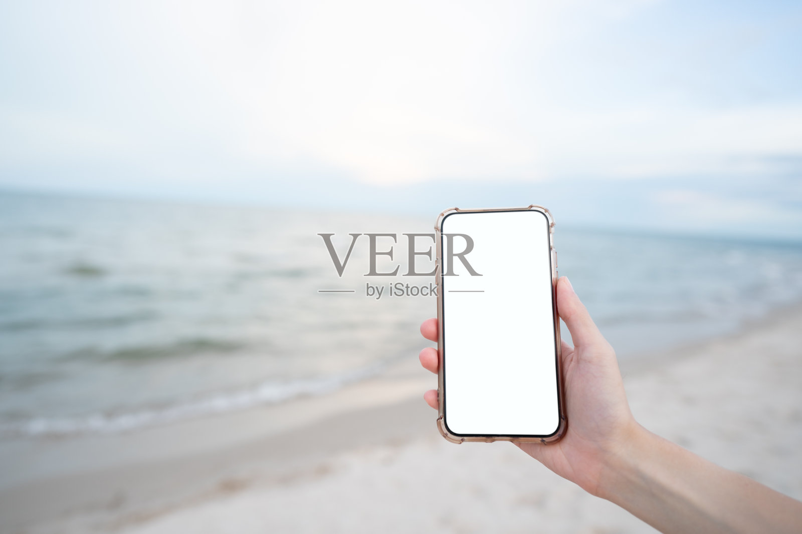 女人手持手机与空白白屏幕模型在海滩上。照片摄影图片