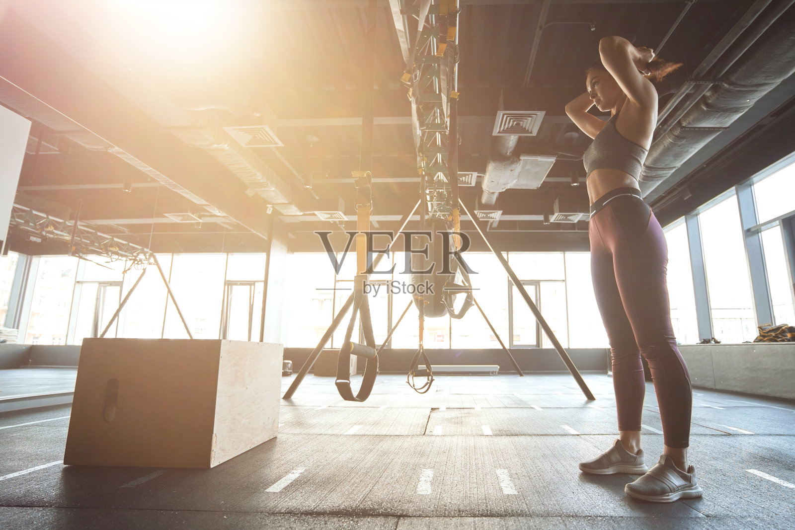 Prepering锻炼。侧面的强壮的运动员妇女在运动服装调整头发,而站在工业健身房,锻炼与trx健身带照片摄影图片