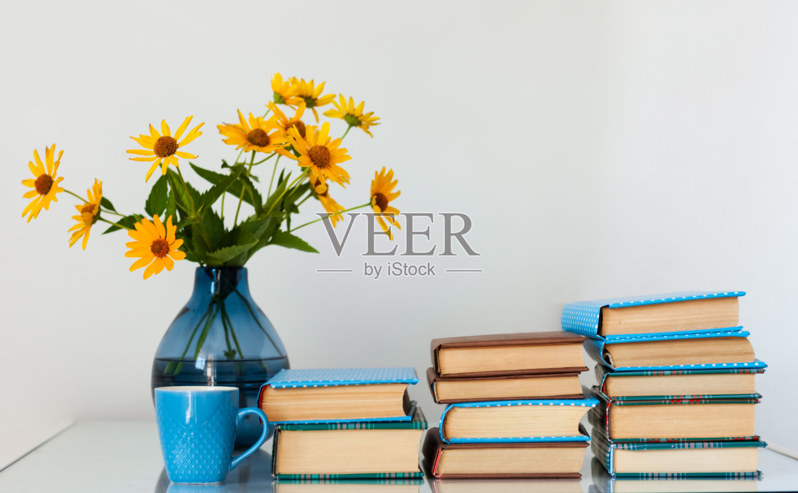 舒适的家庭内部装饰:一堆书和花瓶与黄色的花在桌子上。家庭教育的距离。待在家里的隔离概念照片摄影图片