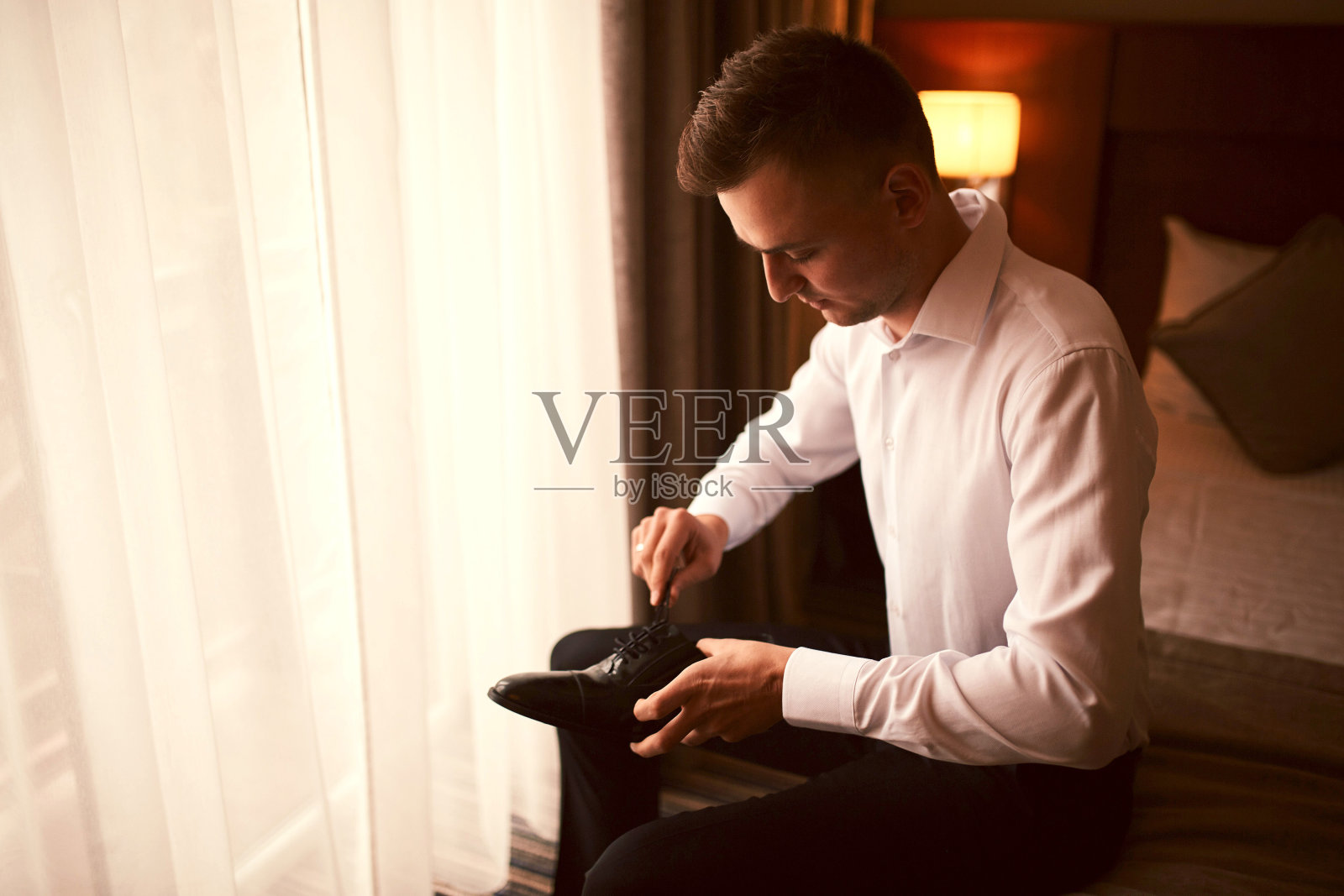 新郎在婚礼前的早晨。新郎早上准备。年轻英俊的新郎穿着结婚鞋照片摄影图片