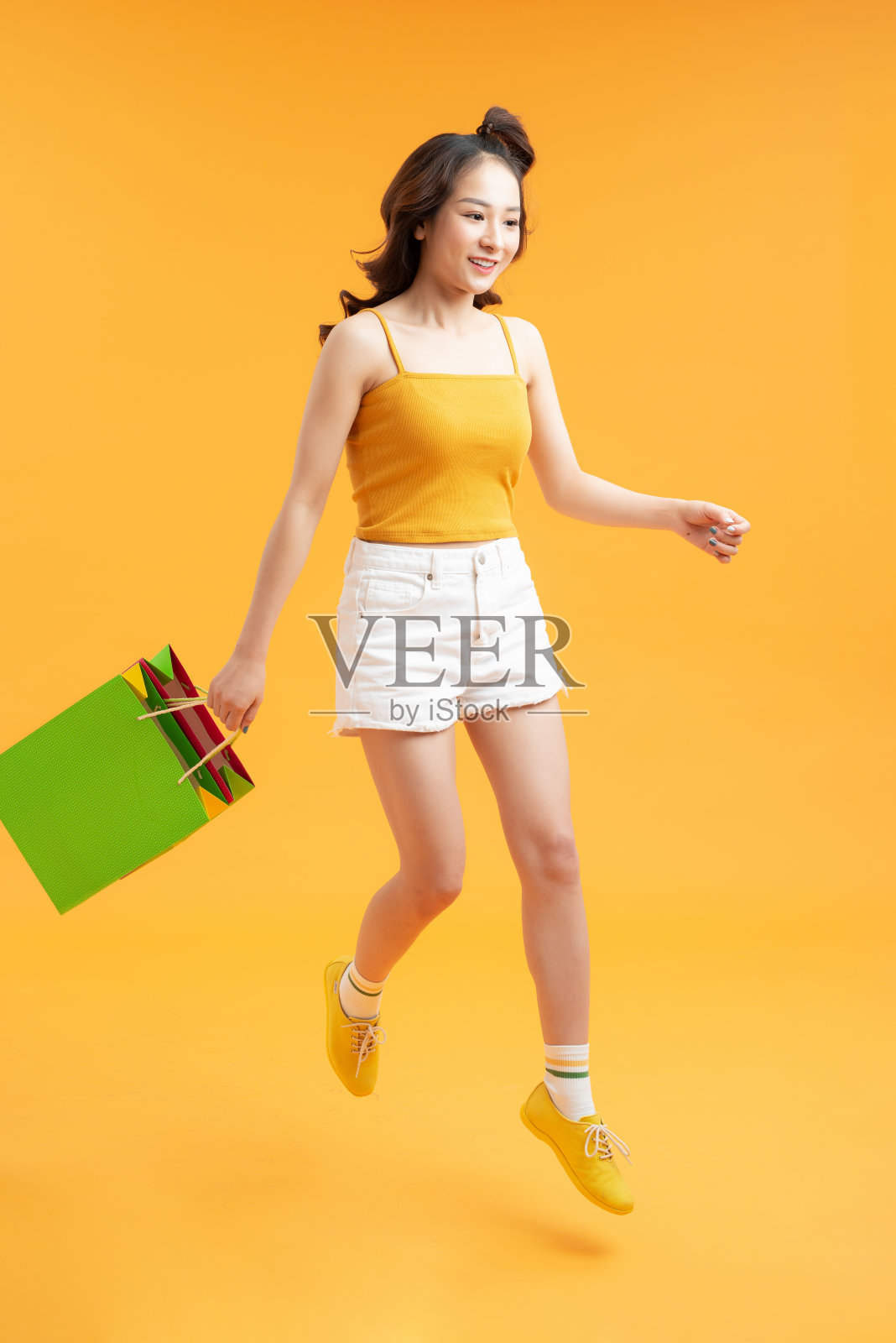 迷人的快乐微笑时尚的女人购物狂跳着跑着拿着购物袋在黄色的背景孤立照片摄影图片