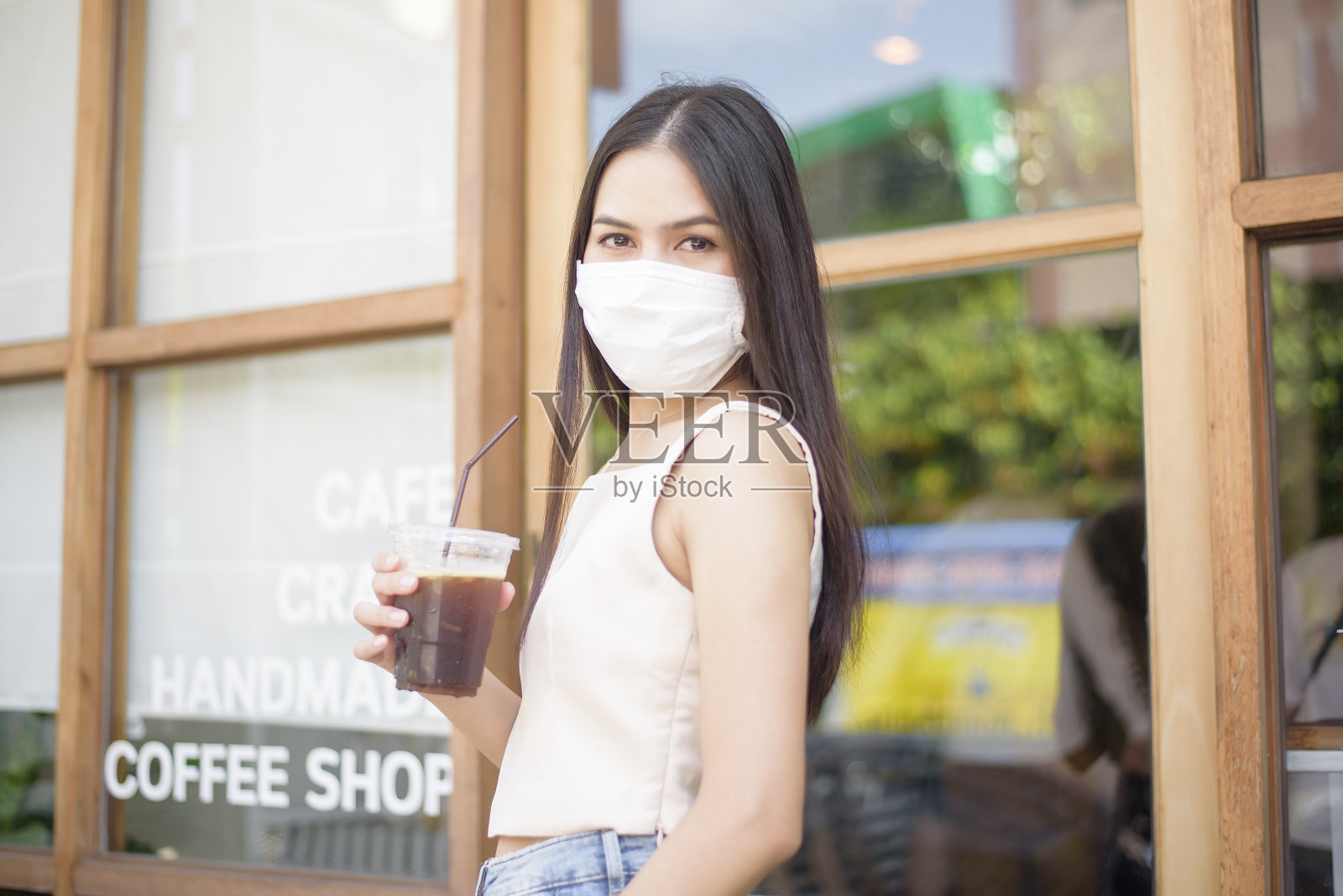一个戴着口罩的漂亮女人在咖啡店前拿着咖啡照片摄影图片