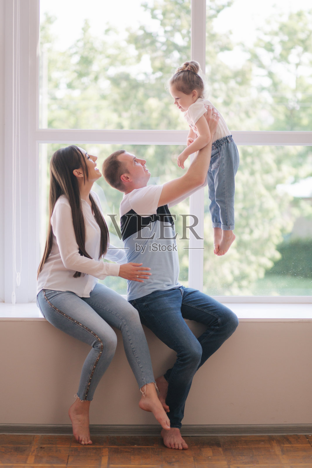 小女孩和爸爸妈妈坐在工作室的大窗户旁。家庭photosession照片摄影图片