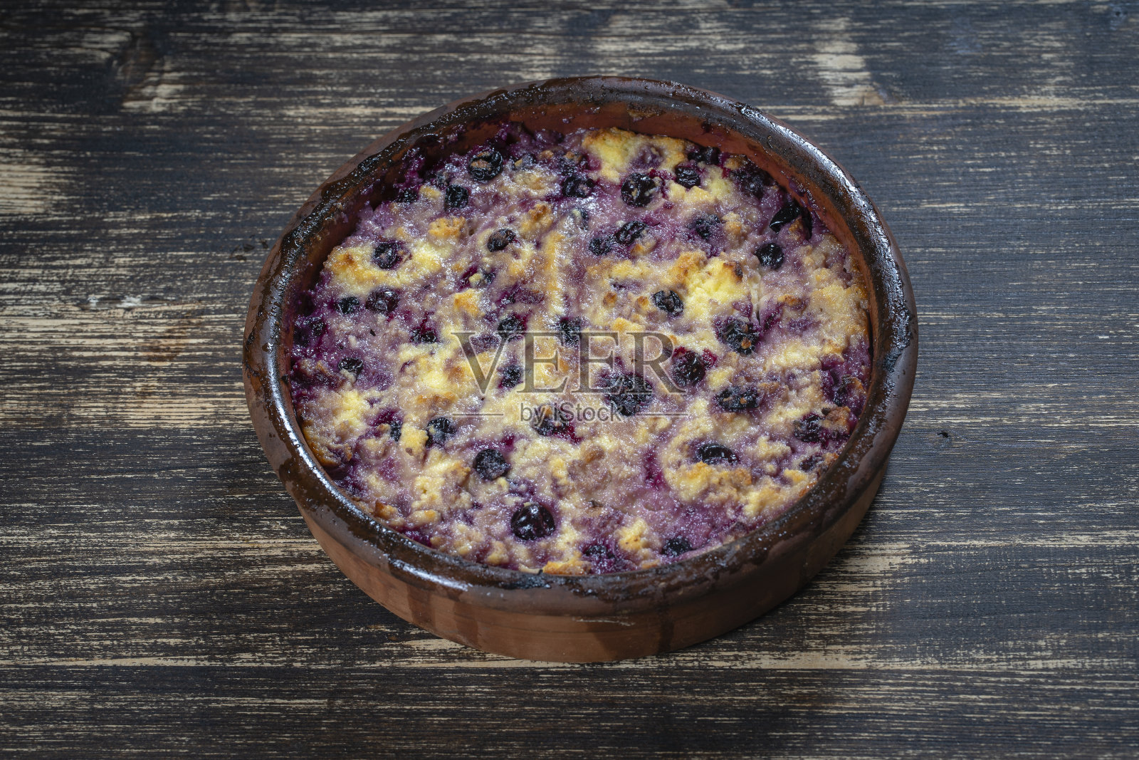 木桌上配有黑醋栗和粗麦粉的甜白干酪砂锅。陶瓷碗配烤白干酪砂锅照片摄影图片