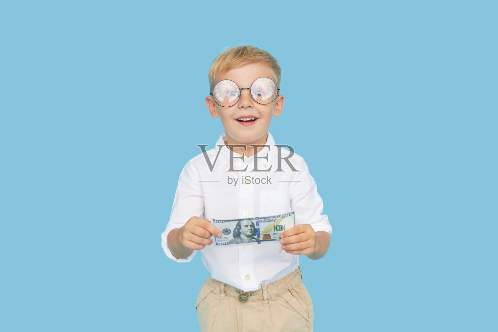 孩子和金钱。戴着眼镜、穿着白衬衫的聪明男孩拿着一张蓝色背景的纸币。儿童教育受益贷款的概念。照片摄影图片