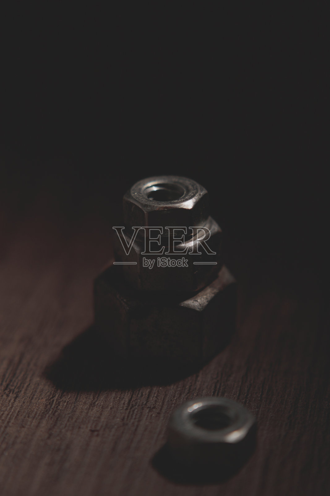 垂直拍摄的金属螺母上的木制表面在黑暗的设置照片摄影图片