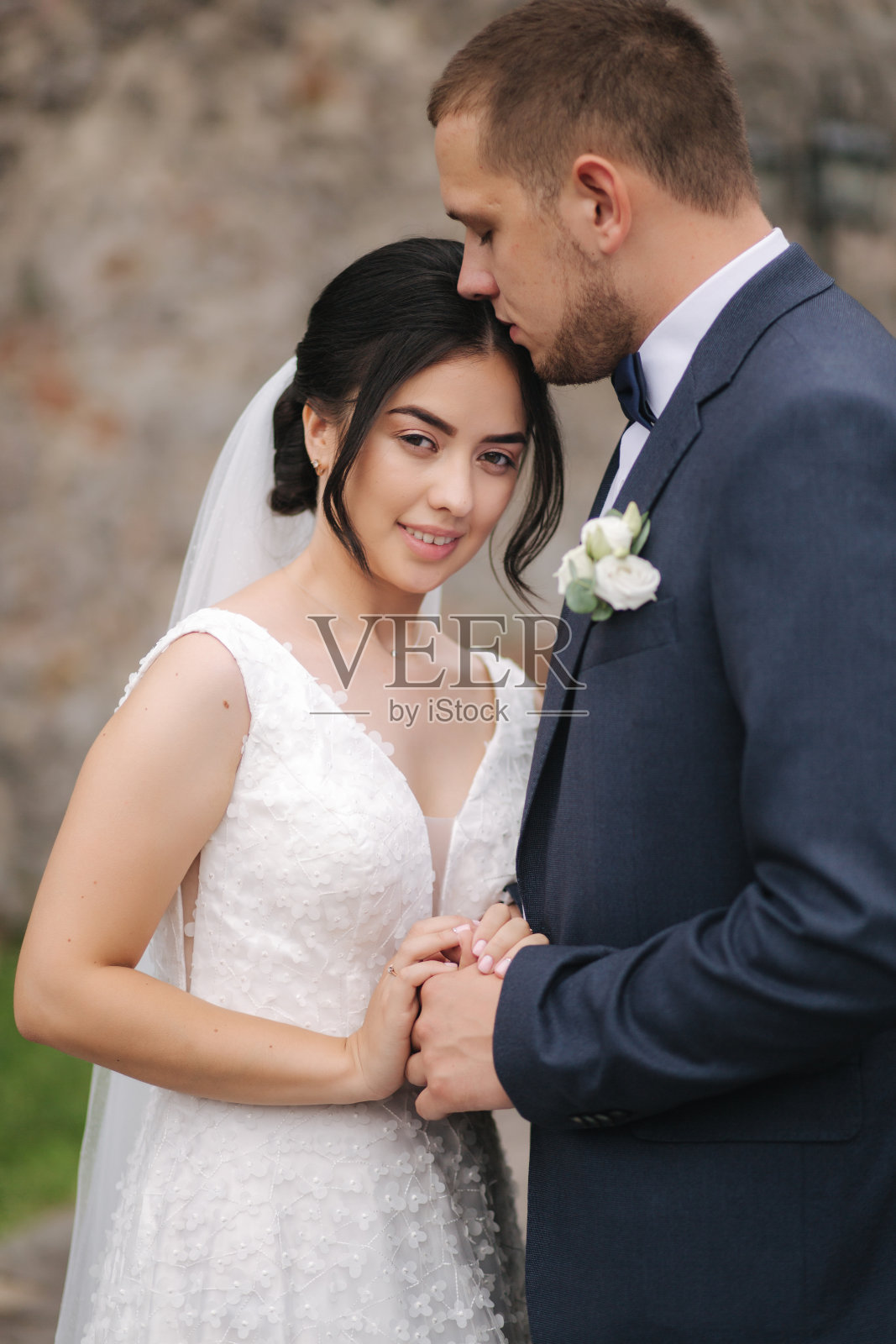 快乐的新婚夫妇走在古老的城堡里,互相拥抱。美丽年轻的新娘和迷人的新郎在石墙前照片摄影图片