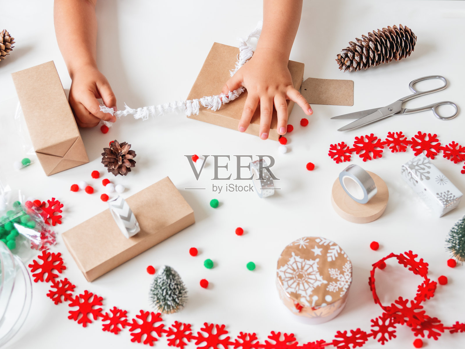 孩子们用牛皮纸包裹手工制作的圣诞礼物,里面有彩色的绒球和雪花丝带。孩子为庆祝新年准备礼物。寒假前的宁静休闲活动。照片摄影图片