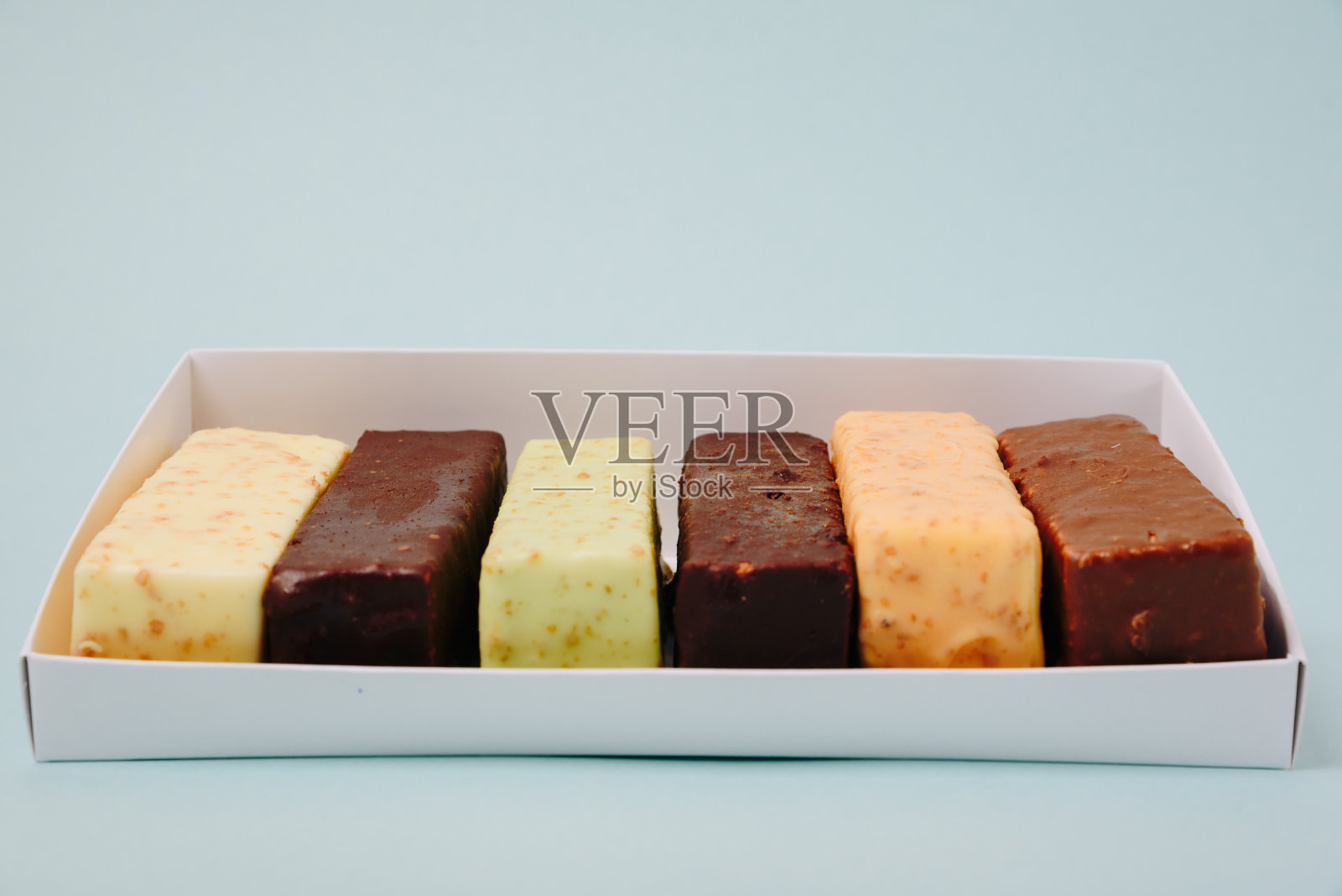 一组蛋糕,涂上糖霜和巧克力,背景很淡照片摄影图片