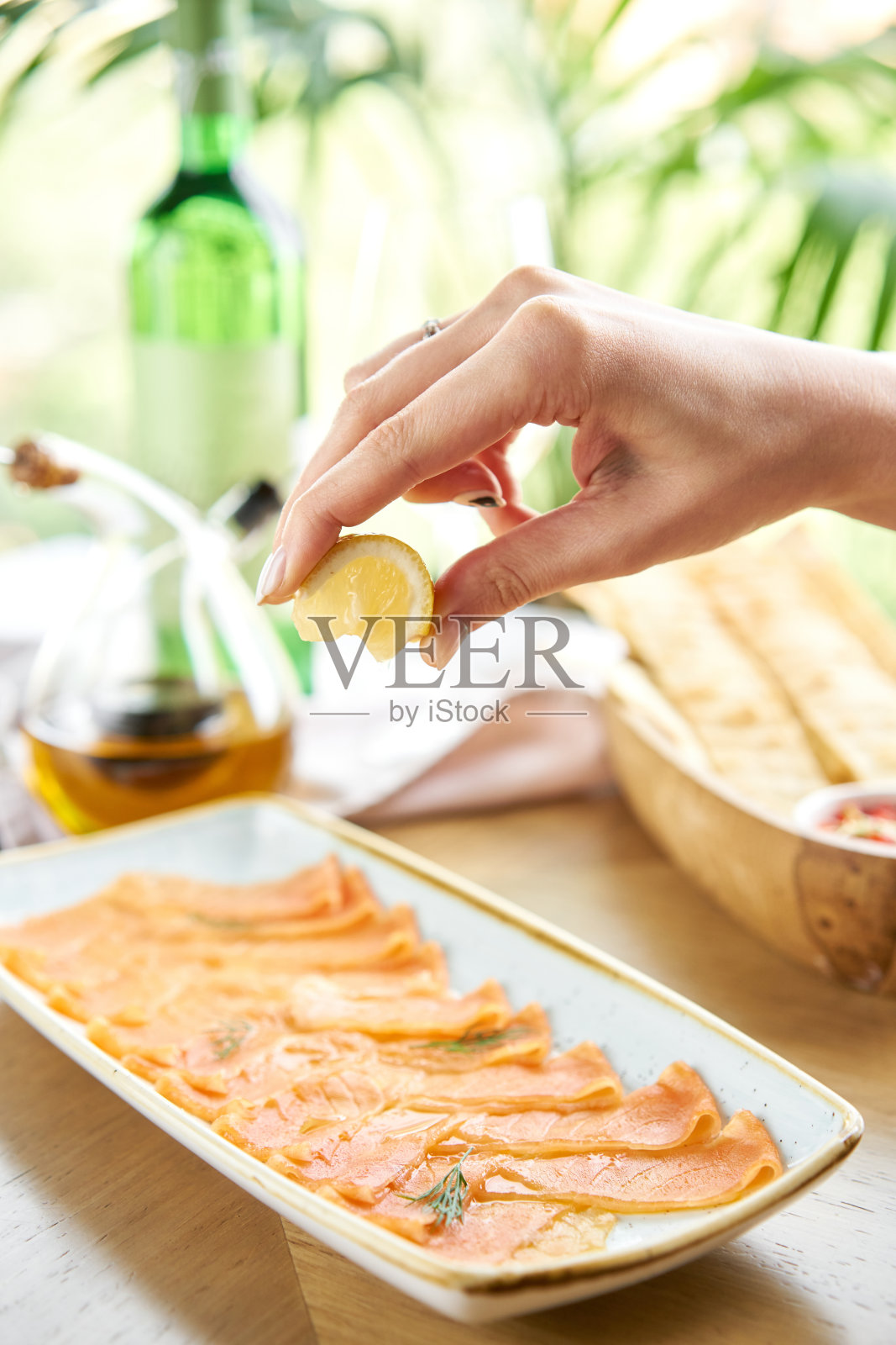 女士们将柠檬汁挤在腌熏鲑鱼或鳟鱼片上。用柠檬切成薄片的红色鱼。餐厅的菜单照片摄影图片