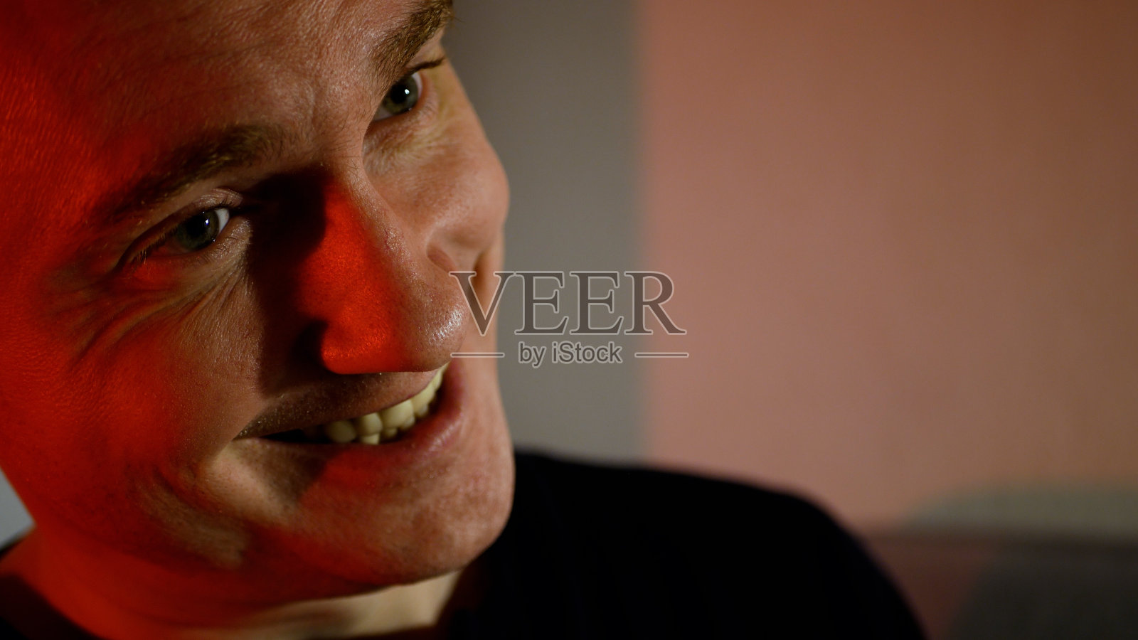 一个神情严肃的年轻人。眉头紧锁,红调邪恶微笑的男人照片摄影图片