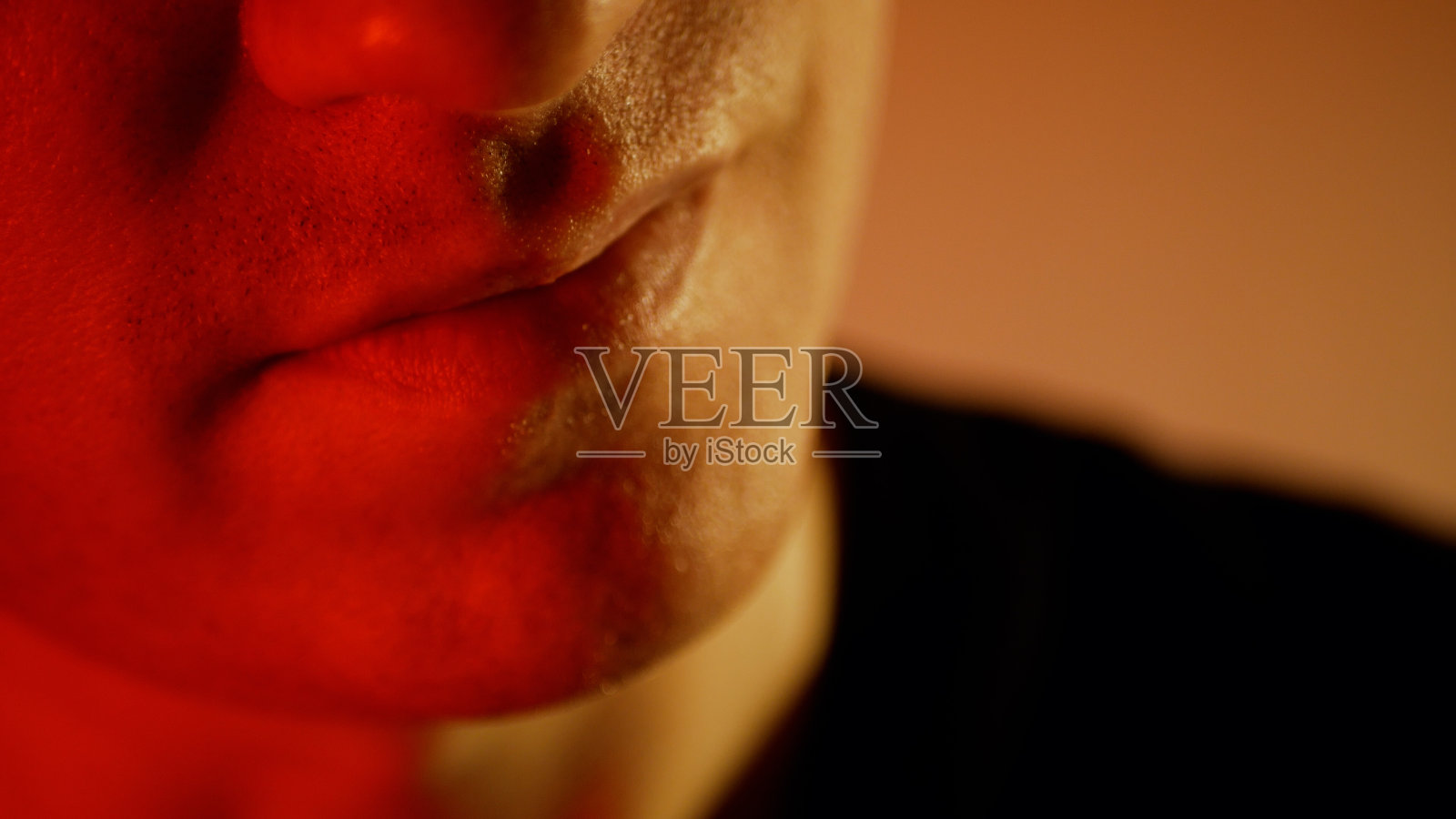 一个神情严肃的年轻人。眉头紧锁,红调邪恶微笑的男人照片摄影图片