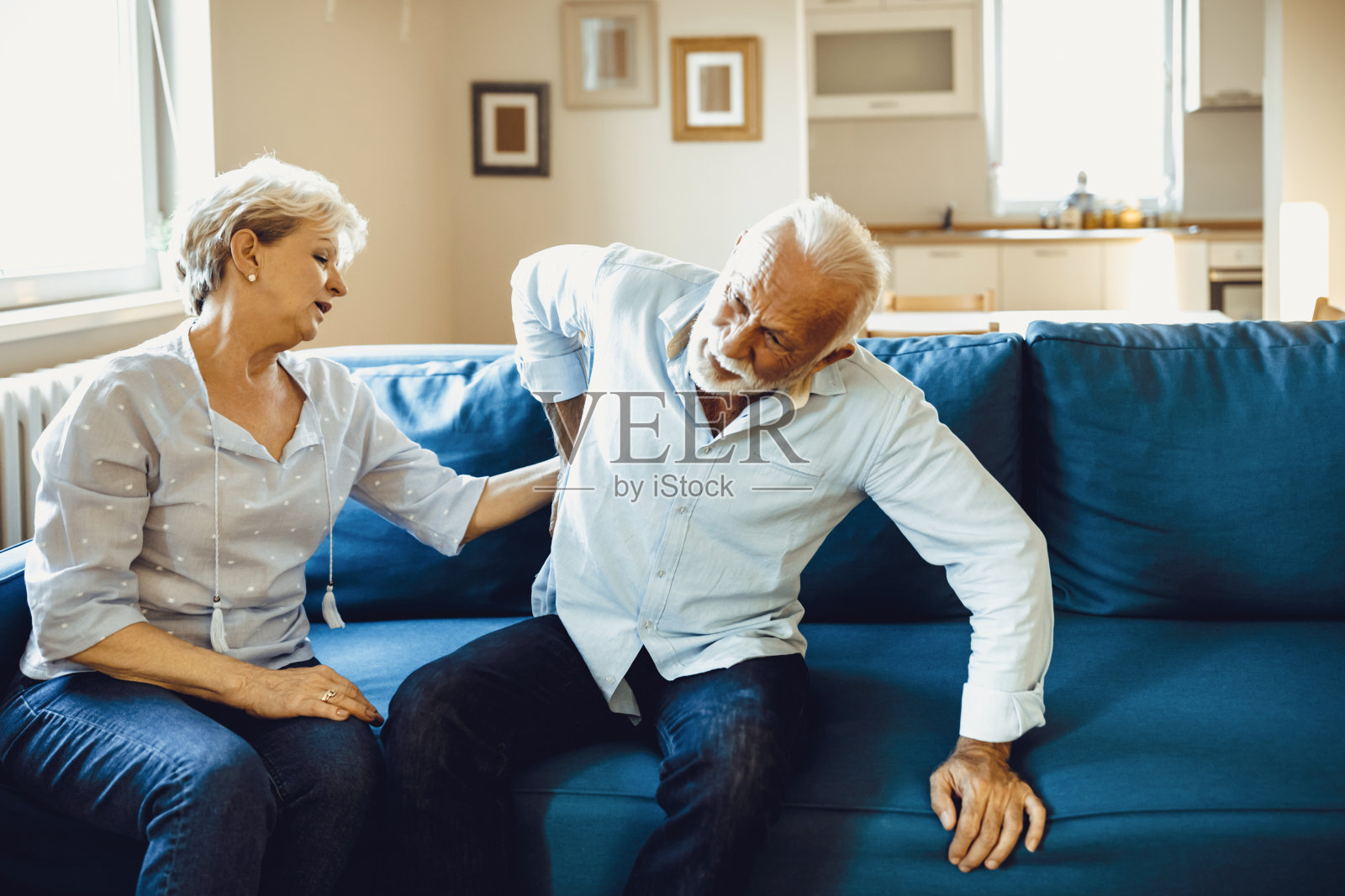 老夫妇在家。英俊的老男人背痛,他的迷人的老女人支持他。照片摄影图片