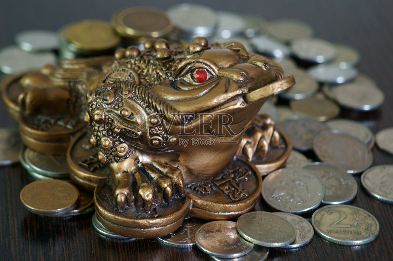 一只金属蟾蜍,旁边是一堆硬币。照片摄影图片