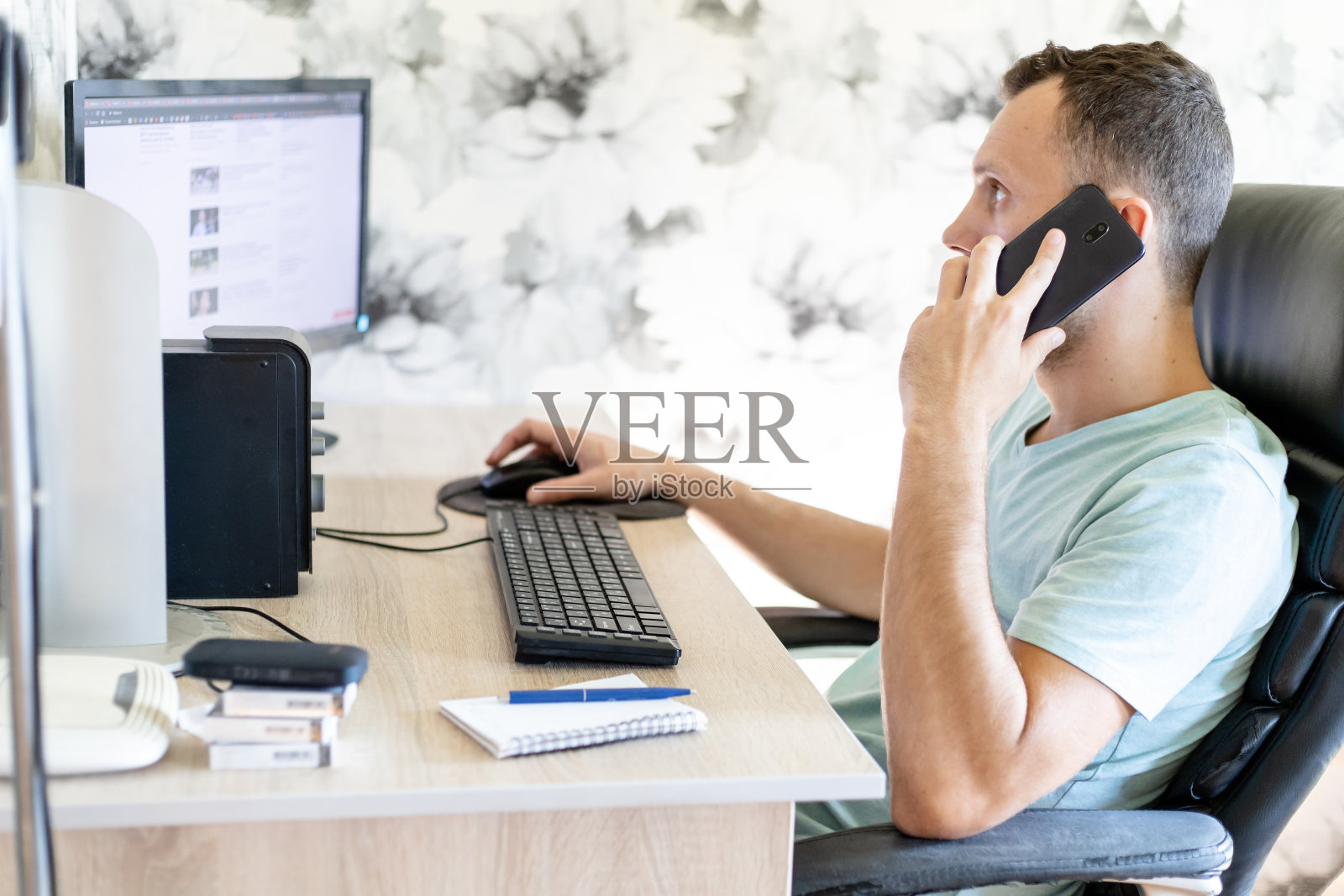 年轻人坐在家里的电脑桌前,通过电话进行远程工作照片摄影图片