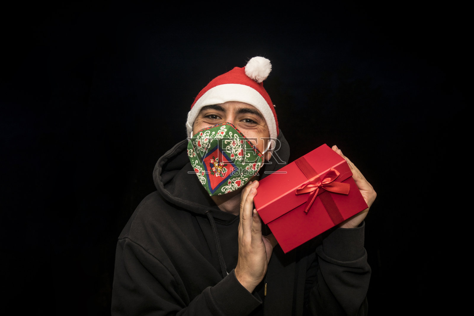 快乐的年轻人戴着防护面具和圣诞帽和摇晃的圣诞礼物照片摄影图片
