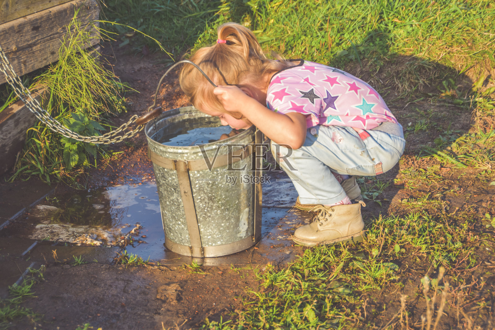 在一个阳光明媚的夏日,一个孩子在井里用水桶汲水,用一个金属杯子喝水照片摄影图片