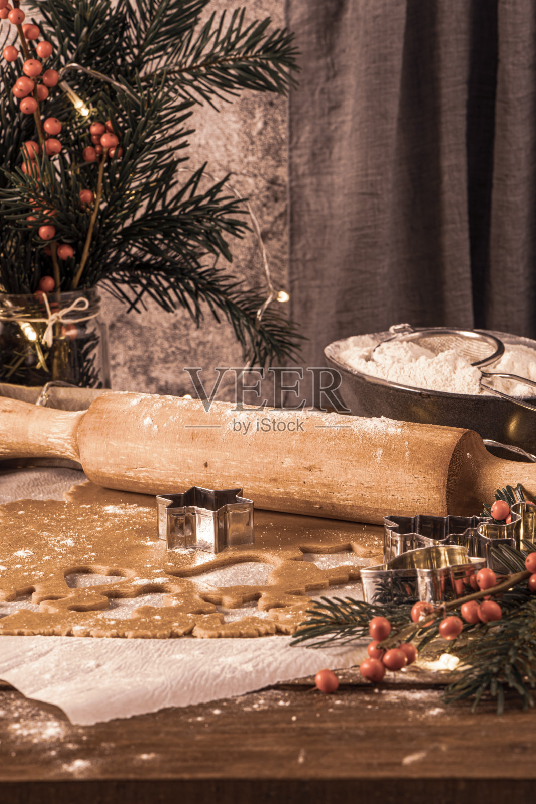 做圣诞姜饼。生面团做成姜饼人、圣诞树、星星、雪花等形状,放在纸盘上,用擀面杖放在质朴的桌子上。准备烤照片摄影图片