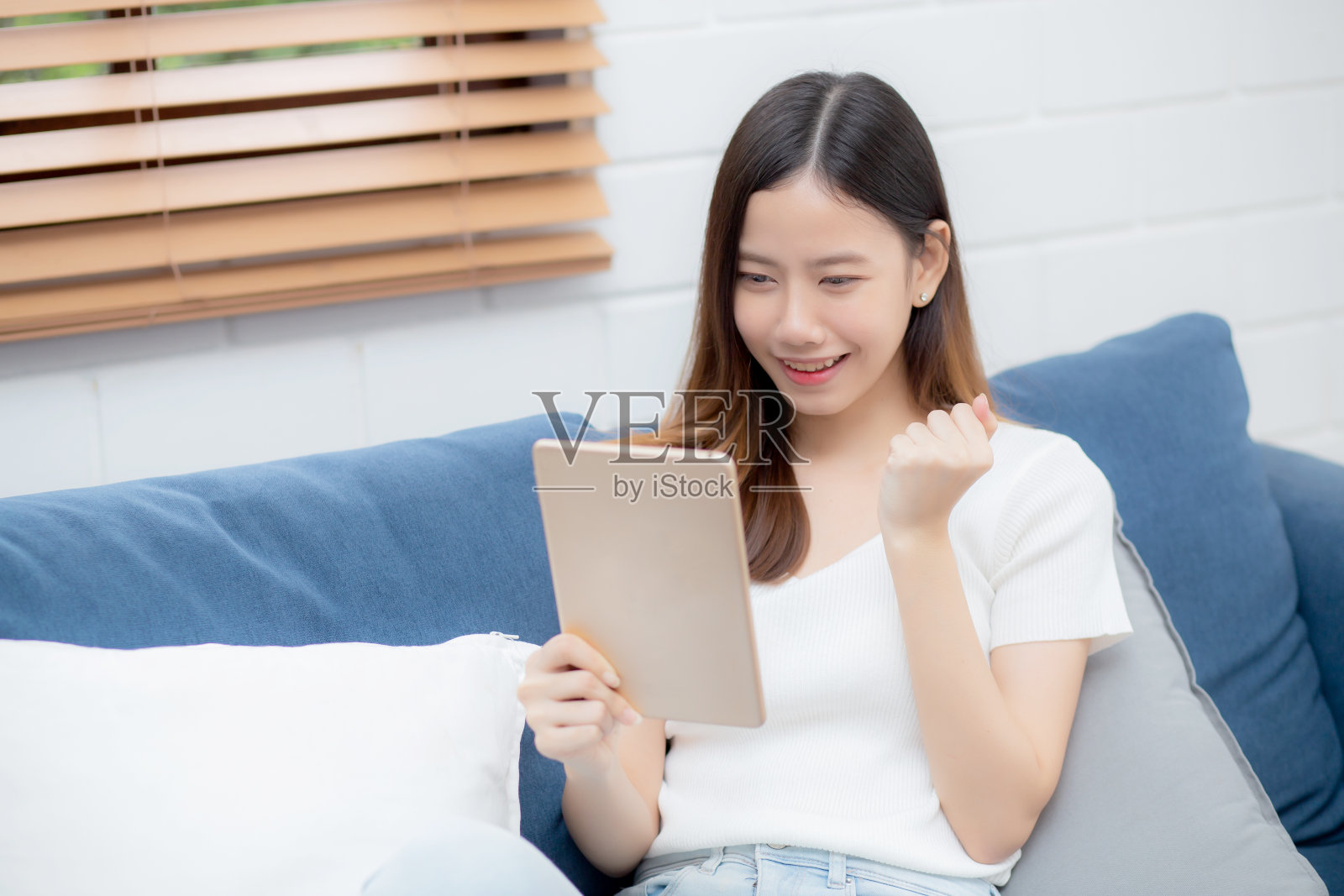 年轻有吸引力的亚洲女人休息使用浏览平板电脑在家里的沙发上,快乐的女孩坐在沙发上放松阅读电子设备兴奋在家里,交流和生活方式的概念。照片摄影图片