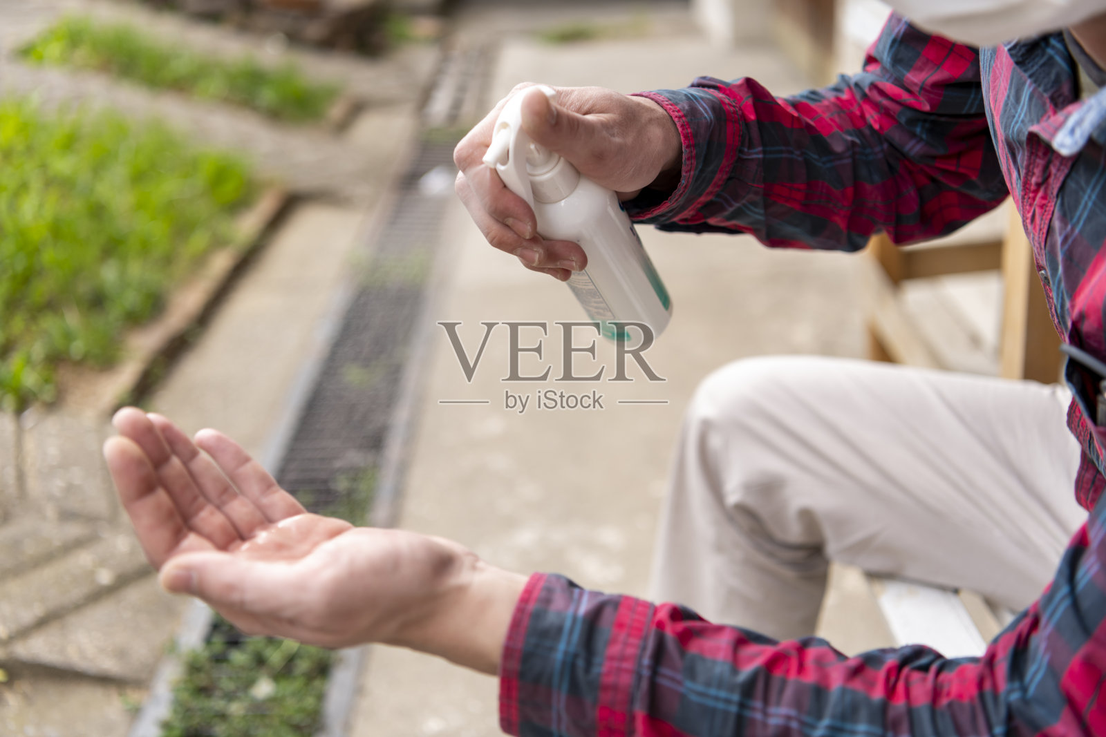 一位带着医用口罩的商人正坐在长凳上用喷雾清洁双手。照片摄影图片