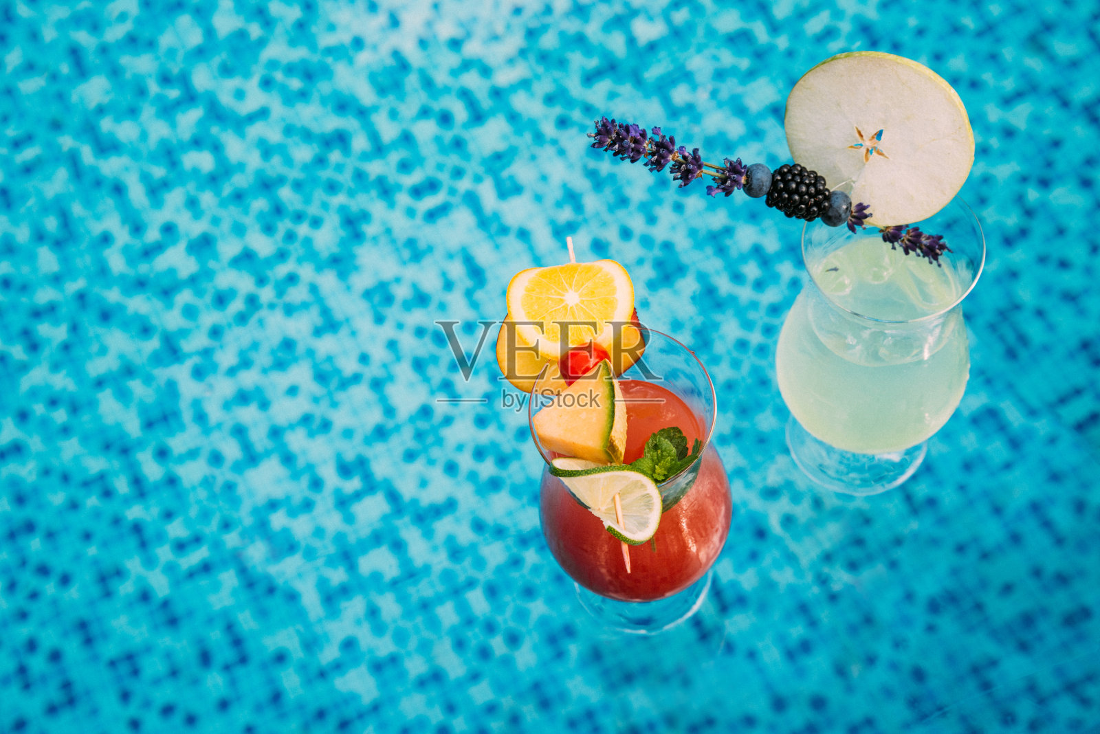 在泳池的透明玻璃托盘上,两杯鸡尾酒正上方照片摄影图片