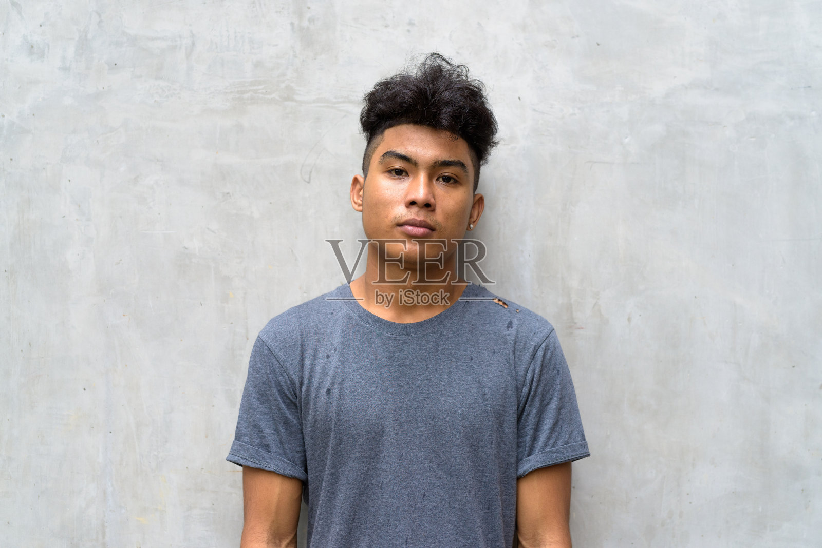 年轻的亚洲男子,一头卷发,靠在户外的混凝土墙上照片摄影图片