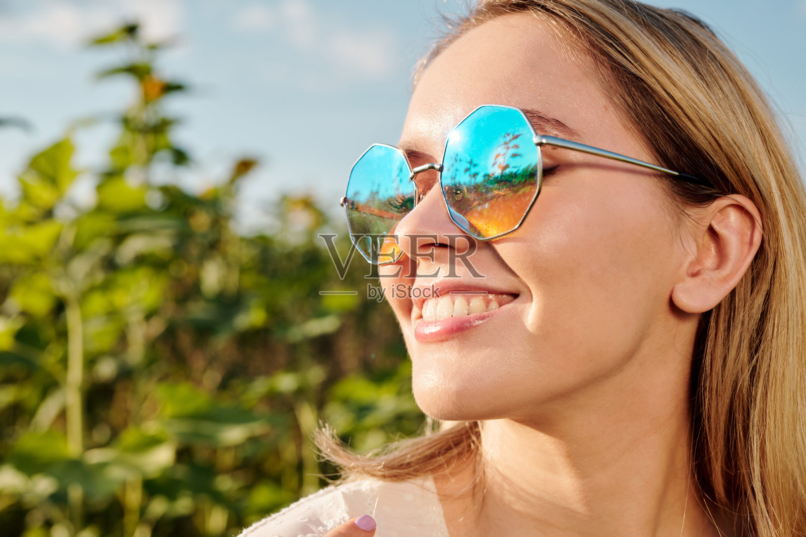 微笑的年轻的金发女人戴着太阳眼镜站在向日葵照片摄影图片